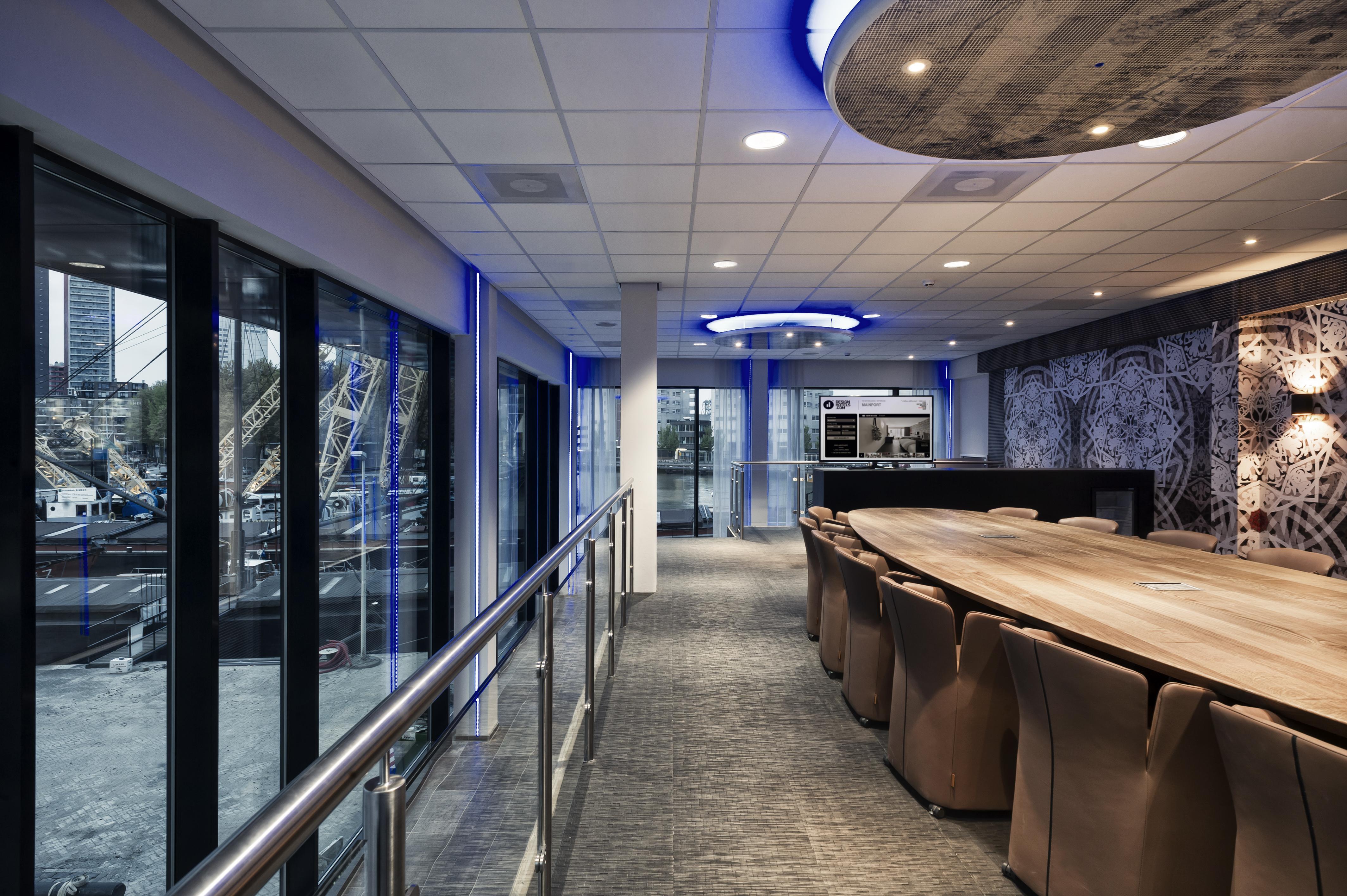Mainport Hotel Rotterdam, A Hilton Affiliate Hotel Εξωτερικό φωτογραφία The photo shows a modern interior space that appears to be a conference room or a meeting area. It features a long wooden table surrounded by brown upholstered chairs. The room has large glass windows that provide a view of the outside, possibly over