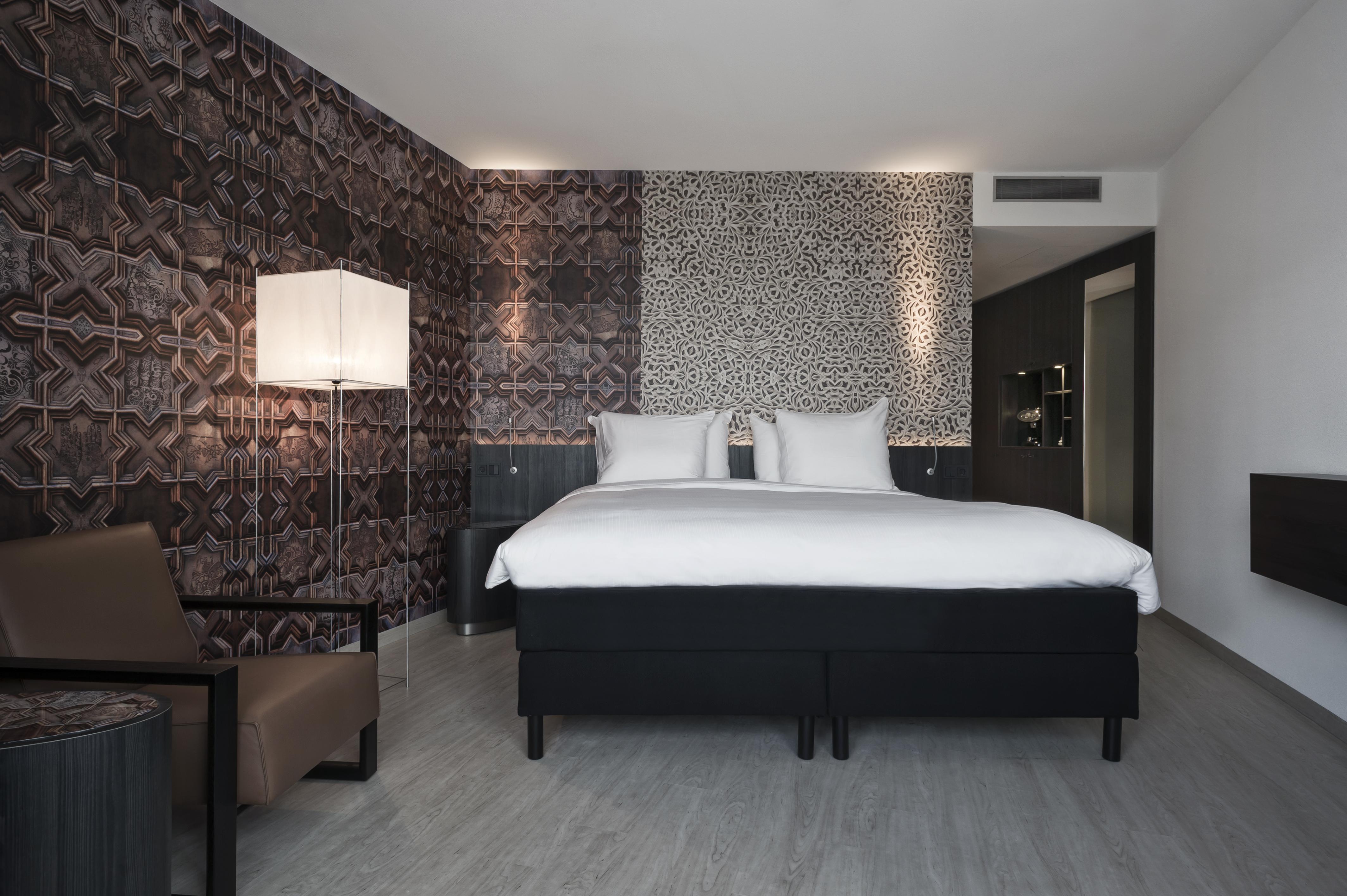Mainport Hotel Rotterdam, A Hilton Affiliate Hotel Εξωτερικό φωτογραφία The photo shows a modern hotel room featuring a large bed with white bedding and two pillows. The walls are adorned with a patterned wallpaper, which adds a decorative touch to the space. On one side of the room, there is a stylish floor lamp providi