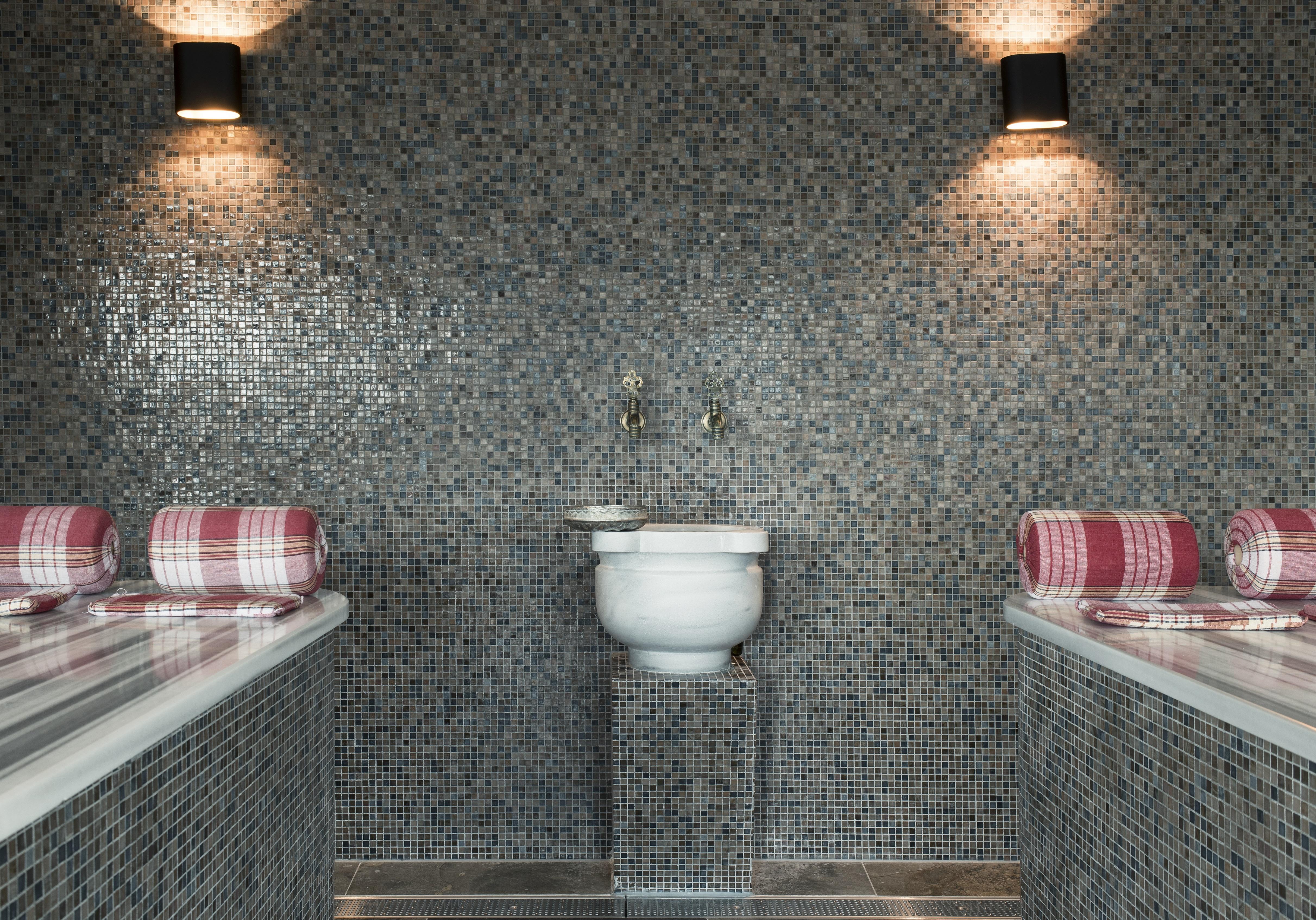 Mainport Hotel Rotterdam, A Hilton Affiliate Hotel Εξωτερικό φωτογραφία The photo shows a modern restroom or spa area with a sleek design. The walls are covered in small, grey mosaic tiles, creating a stylish and contemporary look. There are two bathing areas on either side, each with rolled towels placed on the ledge. I