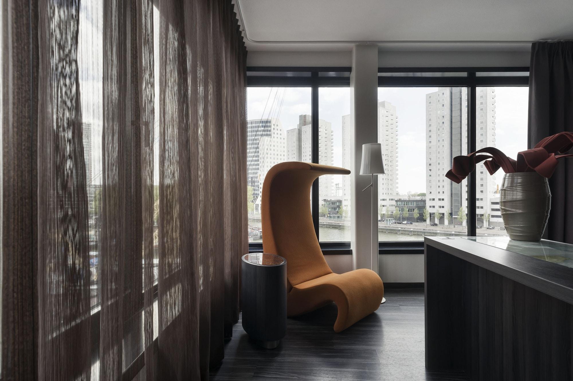 Mainport Hotel Rotterdam, A Hilton Affiliate Hotel Εξωτερικό φωτογραφία The photo shows a modern interior space characterized by a stylish design. In the foreground, there is an eye-catching orange chair with a unique, curved shape. Next to it, there is a small, dark side table. The room features large windows with sheer