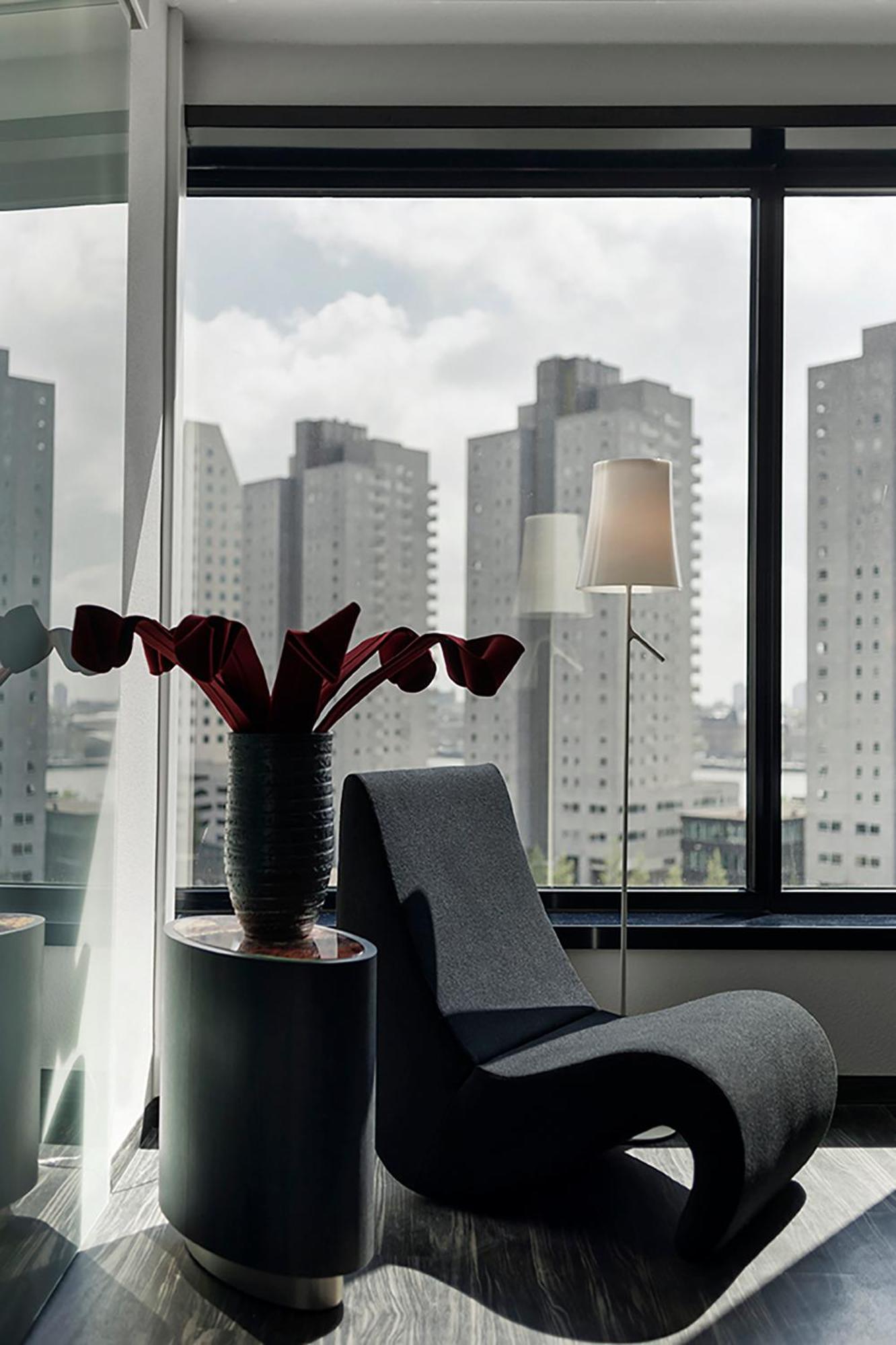 Mainport Hotel Rotterdam, A Hilton Affiliate Hotel Εξωτερικό φωτογραφία The photo shows a modern interior space with a stylish chair and a table featuring a decorative vase. The vase holds large red flowers, creating a striking centerpiece. In the background, there are tall buildings visible through a large window, sugge