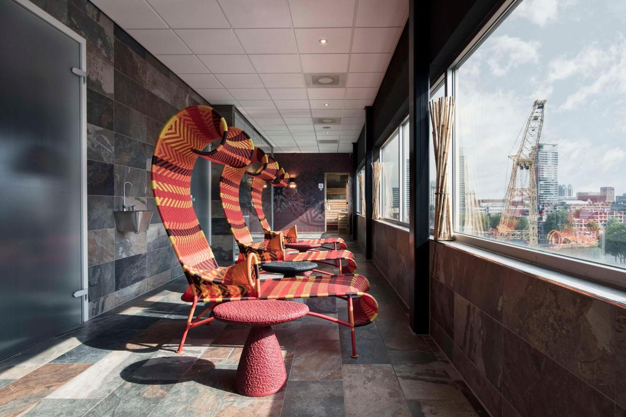 Mainport Hotel Rotterdam, A Hilton Affiliate Hotel Εξωτερικό φωτογραφία The photo showcases a modern and stylish room featuring a series of unique, colorful lounge chairs that have a curved design. These chairs are positioned next to large windows, offering a view of the outside, which includes some cityscape elements an